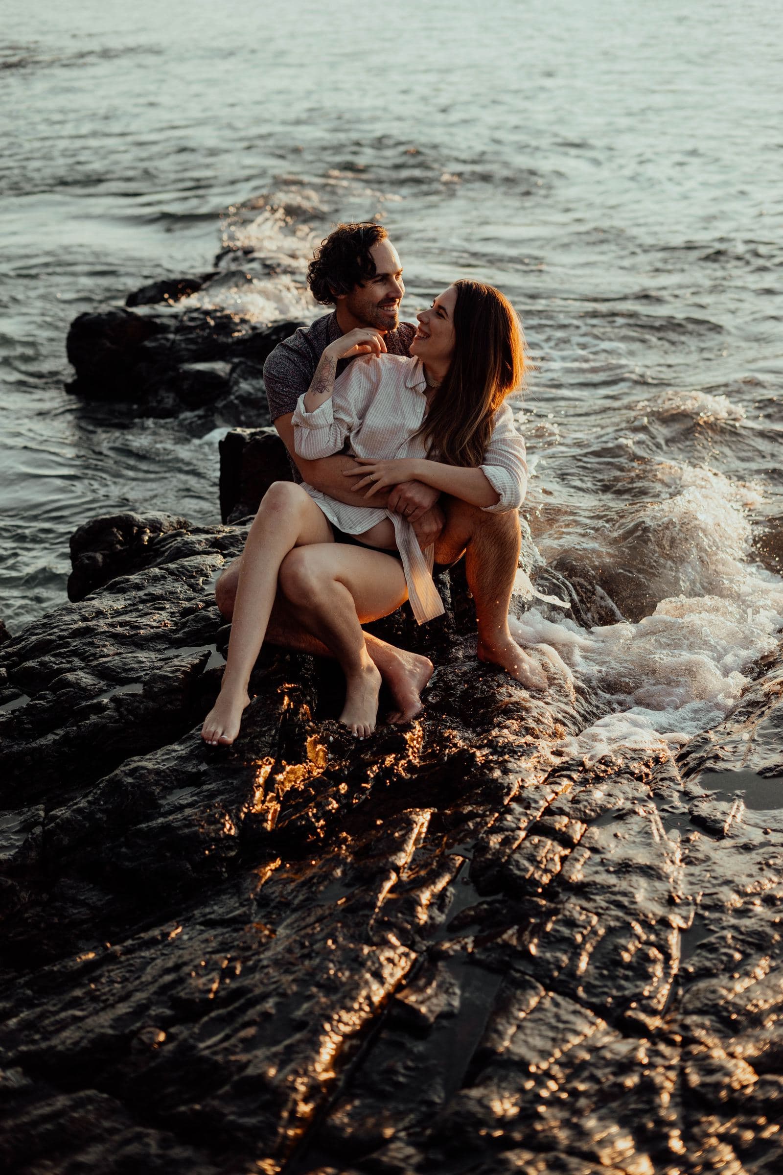 Joe and Jiveny laughing together on the rocks by the ocean