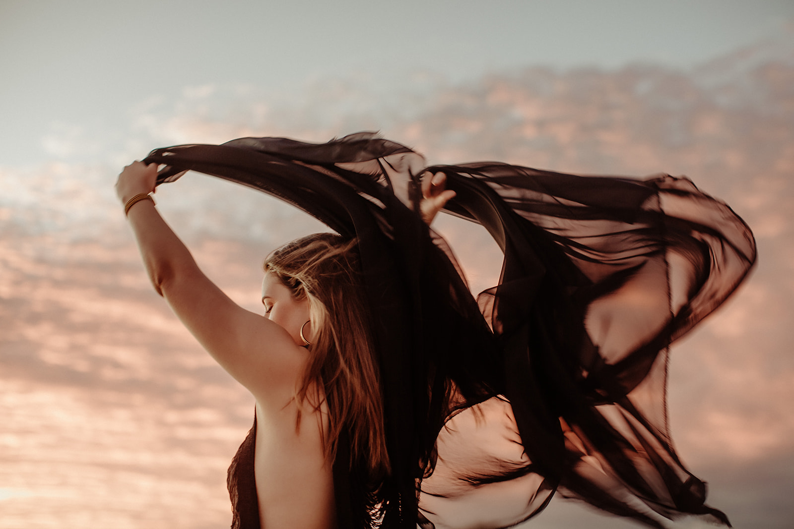 A woman with black silk flowing in the wind at sunset