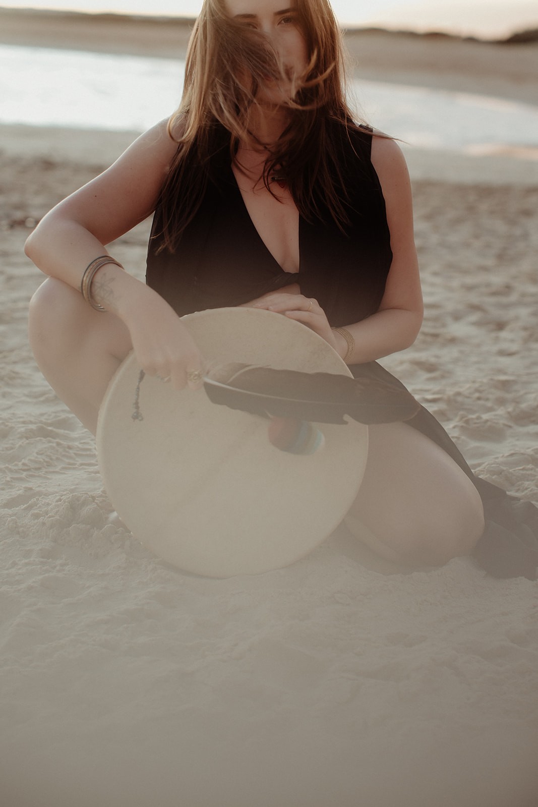 Jiveny sitting in the sand at sunset with a frame drum